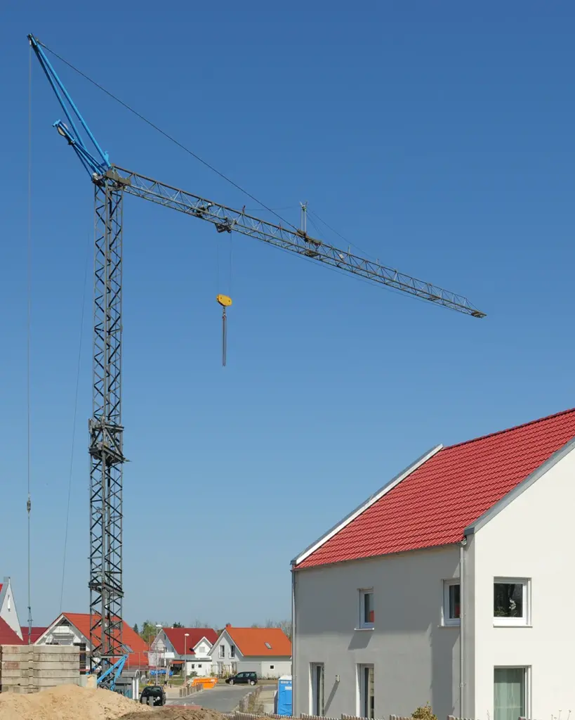 Sinnbild für Unterstützung von Baugutachten durch Heike Schwartz. Das Bild zeigt den Blick über eine Neubausiedlung bei blauem Himmel. Im Fokus liegt ein Baukran auf einer Baustelle.